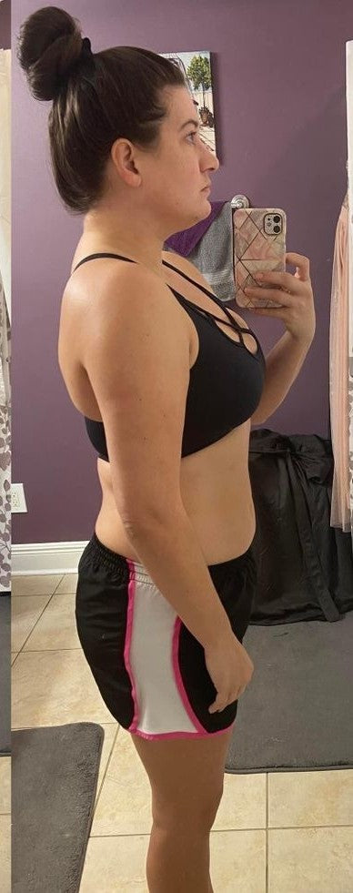 Person taking a mirror selfie wearing a black sports bra and shorts with pink accents.