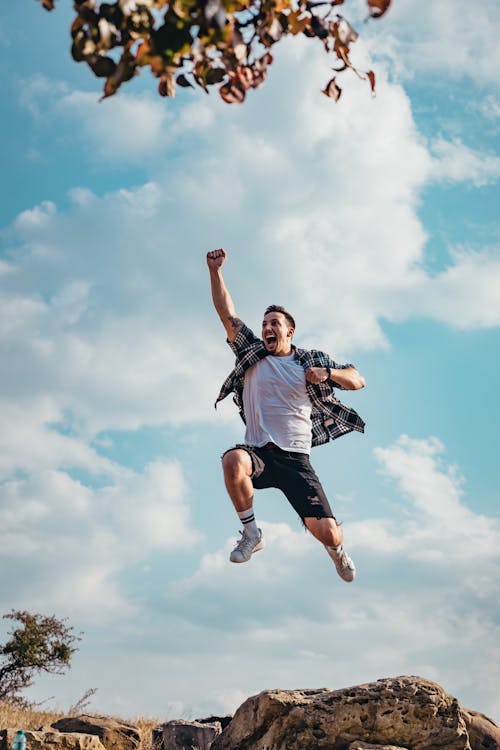Person jumping in the air with a blue sky and clouds in the background