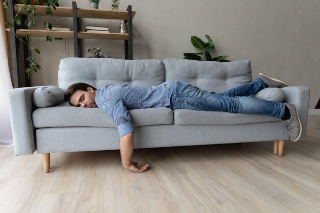 Person lying on a gray sofa in a room with plants and shelves.
