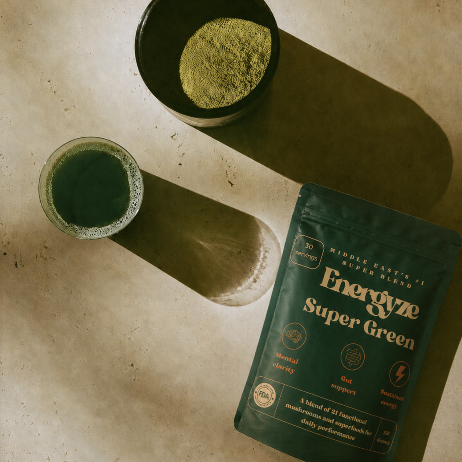 Energyze Super Green powder pouch beside a bowl of green powder and a glass of green drink on a beige surface