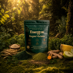 Energyze Super Green powder pouch in a sunlit forest setting surrounded by turmeric root, green apple, broccoli, kale and moringa root